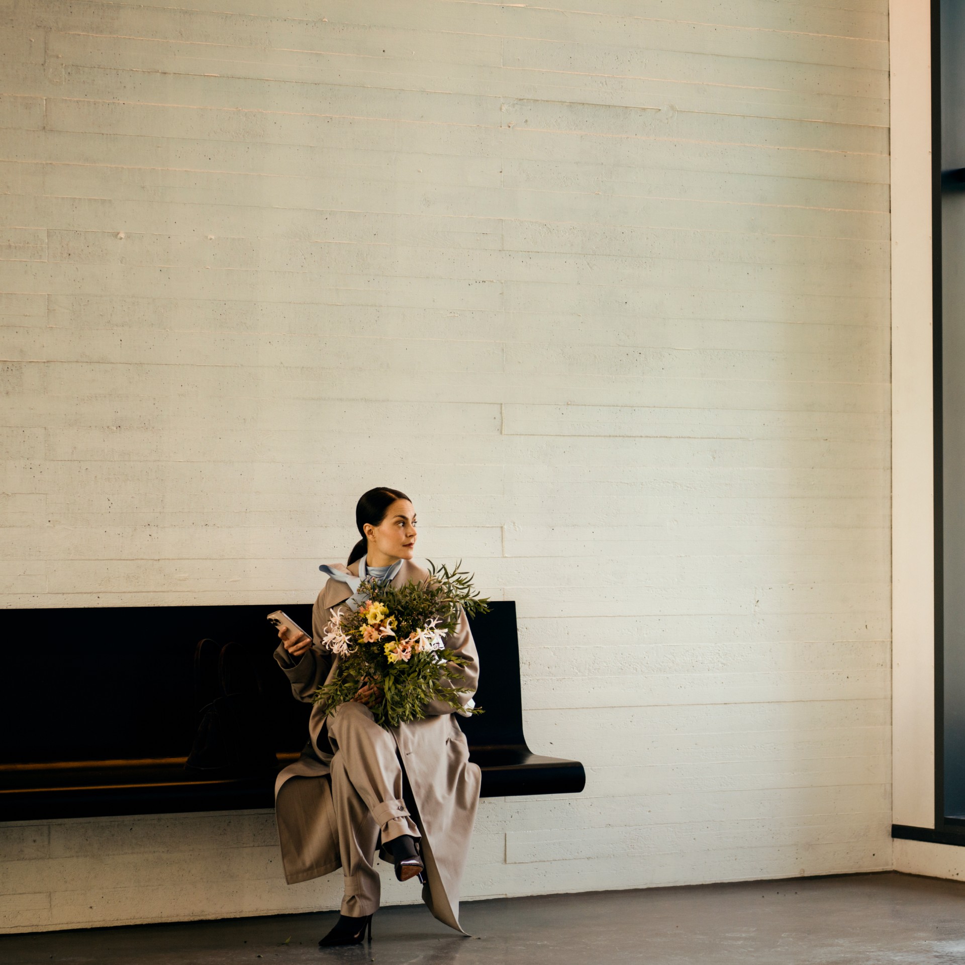 Tyylikäs nainen istuu N&B rakennuksen aulassa puhelin kädessään.